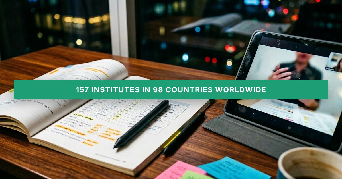 An open German A2 exam prep workbook sits on a modern desk beside a tablet showing a blurred online tutoring session.